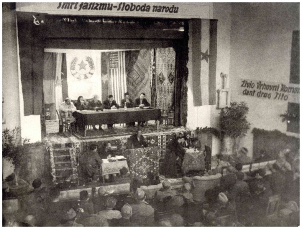 Fotografija Drugog zasjedanja AVNOJ-a, sa delegatima za stolom i publikom u dvorani. Iz Zbirke fotografija HMBIH.