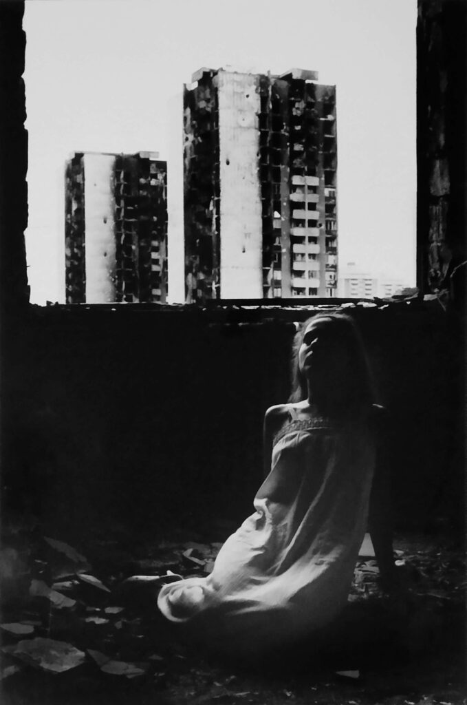 Silueta djevojke u ruševinama s neboderima u pozadini.