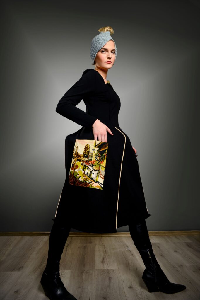 Model u crnoj haljini s torbom s narodnim motivima iz kolekcije “Toplina šare” Ljiljane Majkić, nagrađena na Collegium Artisticum 2023 u kategoriji modnog dizajna