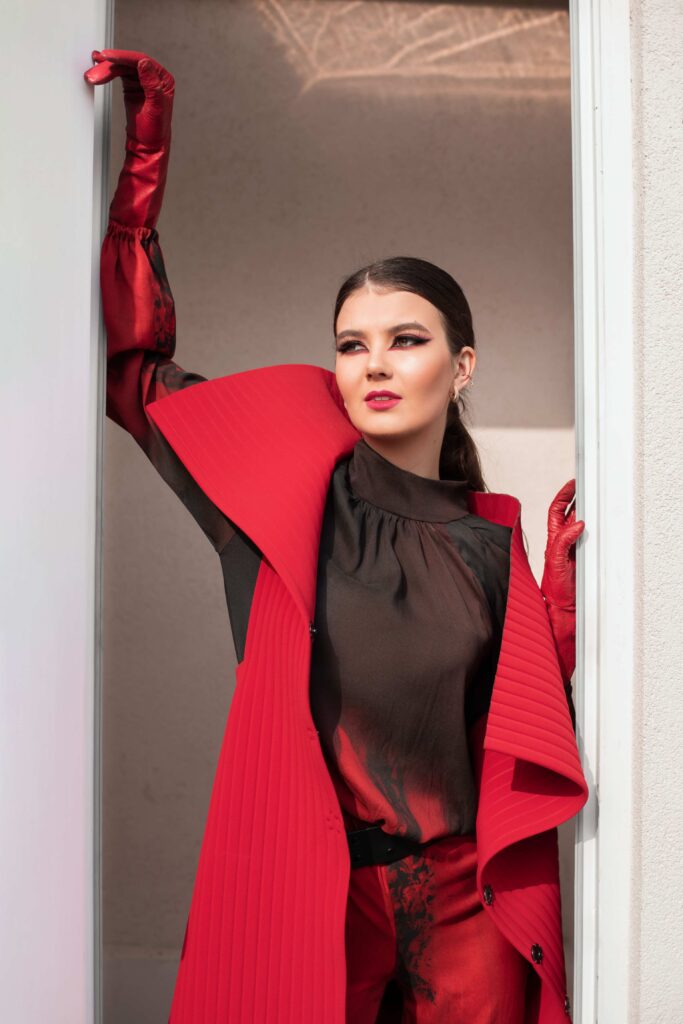 Model u crno-crvenom kaputu s izraženim ramenima i dugim crvenim rukavicama, iz kolekcije “Red” Emine Husedžinović Ibrahimović.