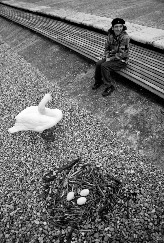 Crno-bijela fotografija “Plodovi revolucije” sa osobom koja sjedi na klupi pored rijeke i labuda, autor Erol Čolaković Šehić, Collegium Artisticum 2021.